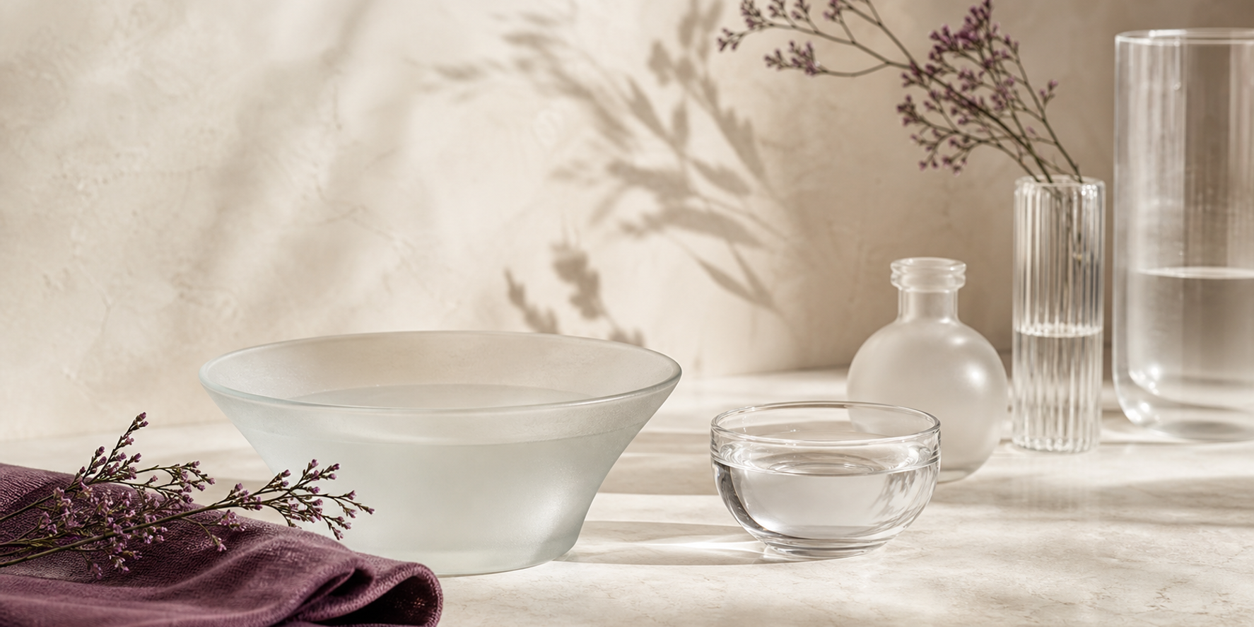 An ivory, clear glass and muted plum cosmetic-routine still life representing the KLAPP Purify range.